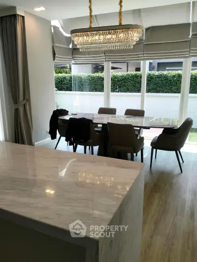 Elegant dining area with chandelier and garden view, featuring a marble countertop and modern decor.