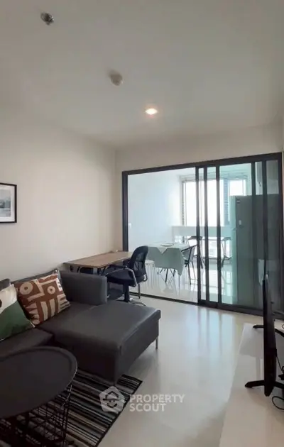 Modern living room with sleek furniture and glass partition leading to dining area.