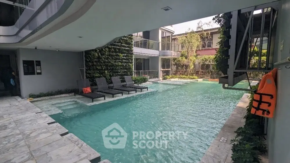 Luxurious modern pool area with sun loungers and lush greenery in a contemporary residential complex.