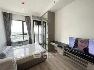 Modern bedroom with large window and city view, featuring a TV and stylish furniture.
