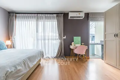 Spacious bedroom with modern decor and natural light, featuring a cozy workspace.