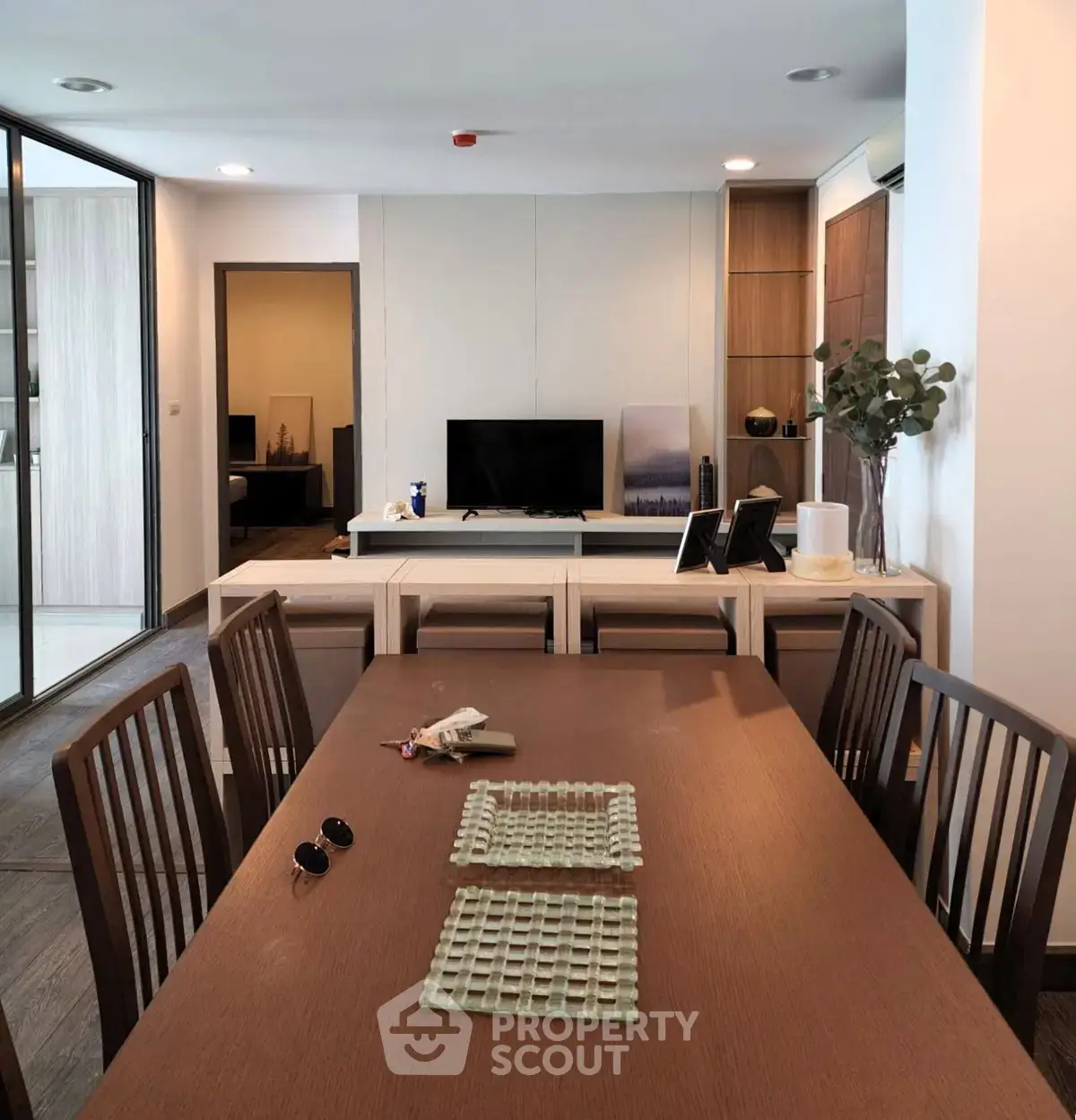 Modern dining area with wooden table and chairs, open layout leading to cozy living room with TV.
