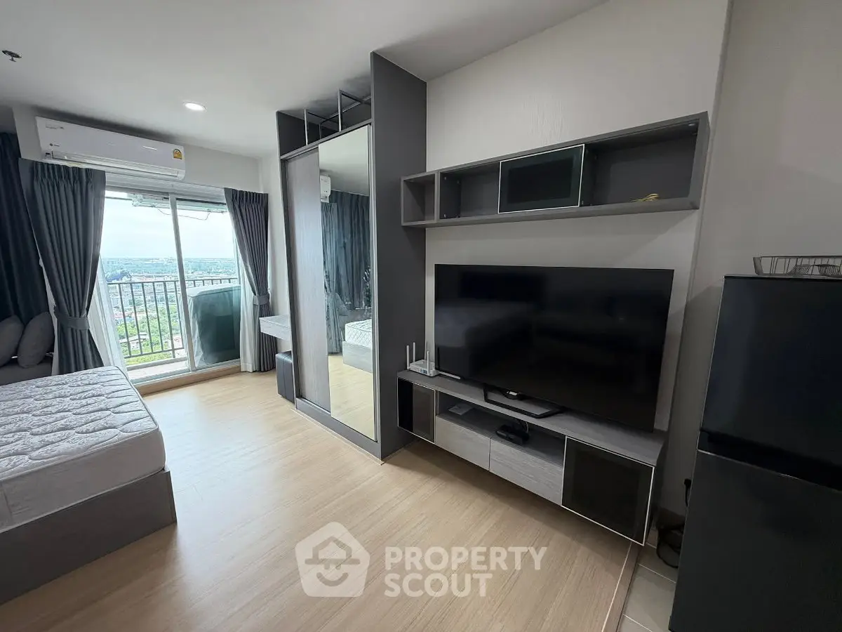 Modern studio apartment with large TV, balcony view, and sleek furnishings.
