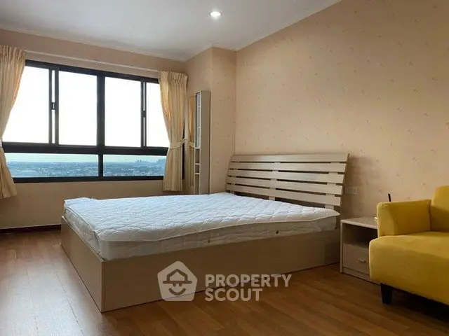 Spacious bedroom with large window and wooden flooring, offering a serene view.