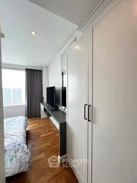 Modern bedroom with sleek wardrobe and city view, featuring a stylish TV setup and elegant wooden flooring.