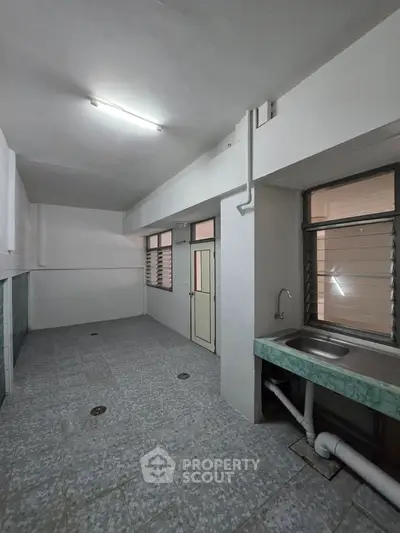 Spacious utility area with tiled flooring and sink, ideal for laundry or storage in a residential property.