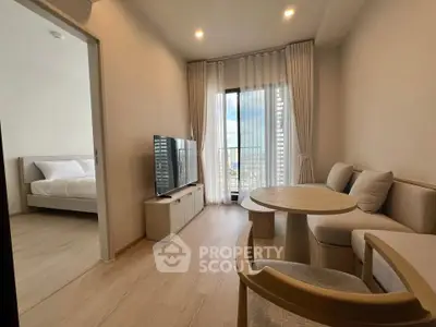 Modern living room with natural light and city view, featuring cozy seating and a large TV, adjacent to a bedroom.