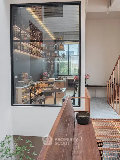 Modern home with a spacious, open-layout kitchen visible through large glass windows, complemented by warm wooden accents and a sleek staircase, embodying contemporary elegance.
