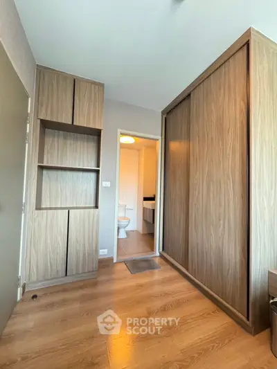 Modern bedroom with wooden flooring and built-in wardrobe, leading to a bathroom.