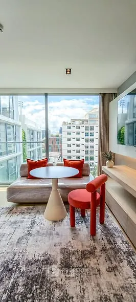 Modern living room with floor-to-ceiling windows and city view, featuring stylish furniture and vibrant decor.