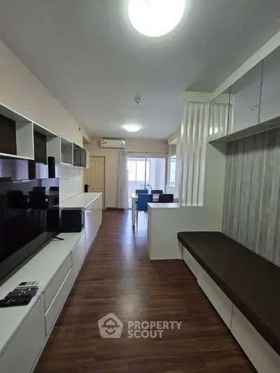 Modern living room with sleek furniture and dining area, featuring wood flooring and ample natural light.