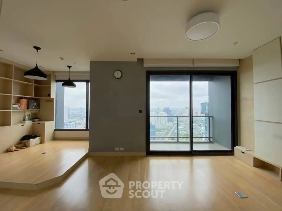 Spacious modern living room with large windows and city view, featuring wooden floors and built-in shelves.