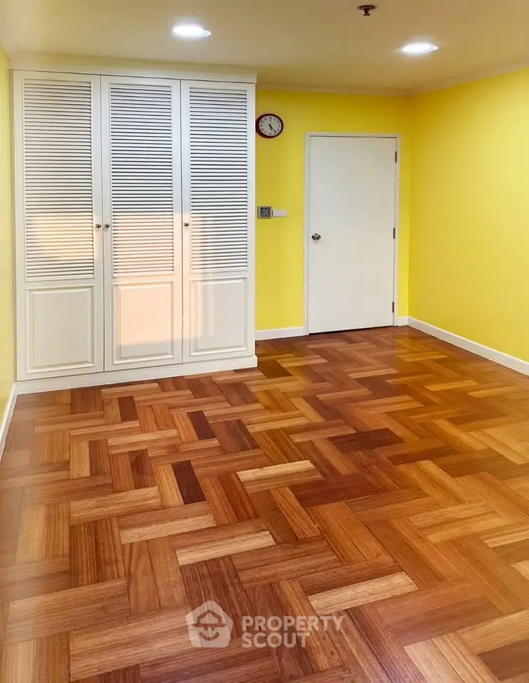 Spacious room with vibrant yellow walls and elegant parquet flooring, featuring a built-in wardrobe.