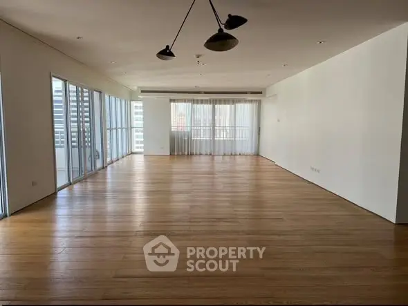 Spacious empty living room with wooden floors and large windows in modern apartment.