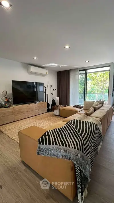 Spacious living room with modern decor and large window overlooking greenery, featuring a cozy sectional sofa and flat-screen TV.