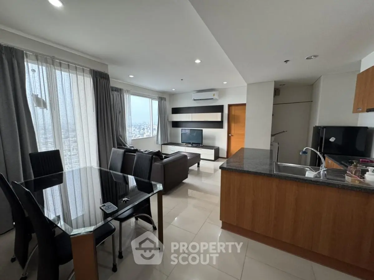 Modern open-layout living room with dining area and kitchen, featuring sleek furniture and large windows.