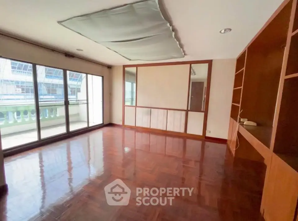 Spacious living room with wooden flooring and large windows opening to a balcony.