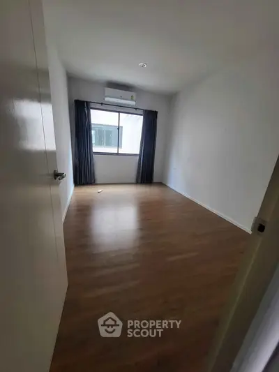 Spacious empty bedroom with wooden flooring and large window, perfect for customization.