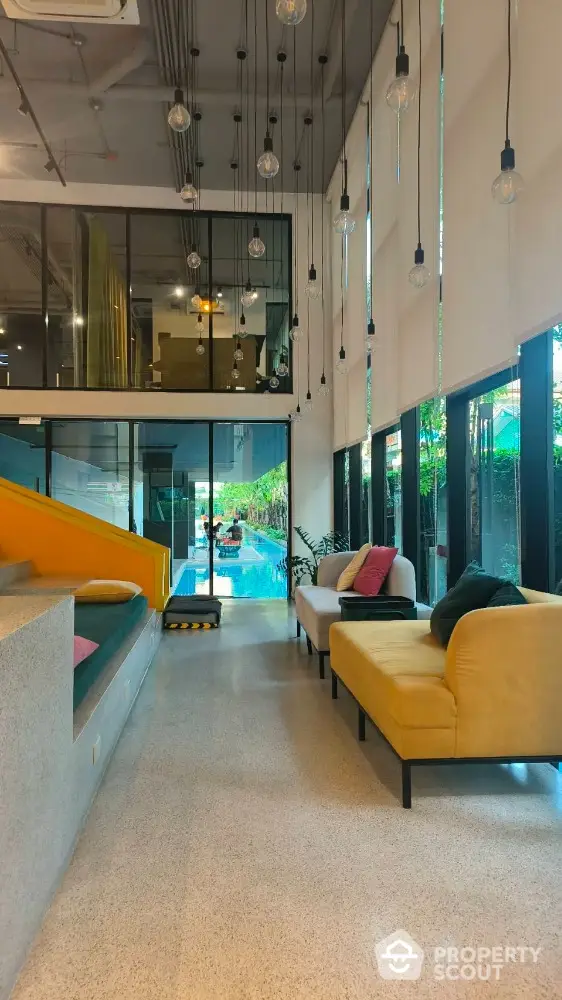 Modern living room with high ceilings and pool view, featuring stylish seating and hanging lights.