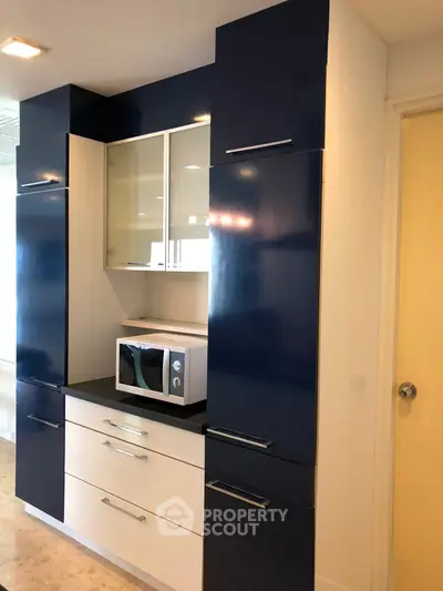 Modern kitchen with sleek cabinetry and built-in microwave, featuring a stylish blue and white color scheme.