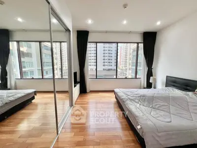 Spacious bedroom with large windows and city view, featuring wooden floors and modern decor.