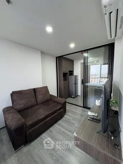 Modern living room with sleek design and balcony view, featuring a cozy sofa and flat-screen TV.