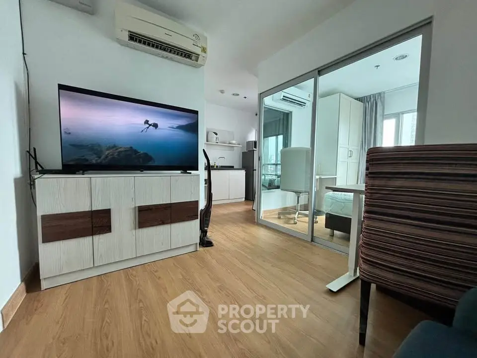 Modern living room with wooden flooring, large TV, and mirrored closet doors in a stylish apartment.
