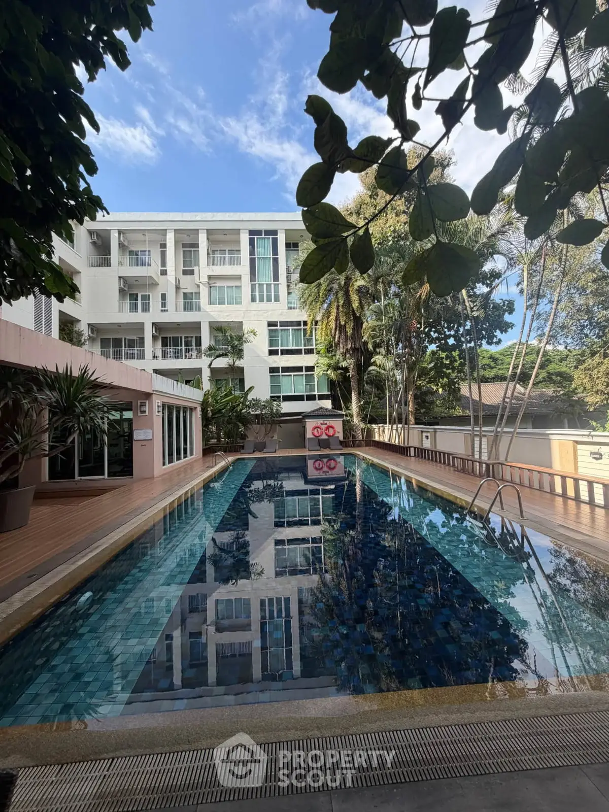 Luxurious residential building with a stunning outdoor pool surrounded by lush greenery.