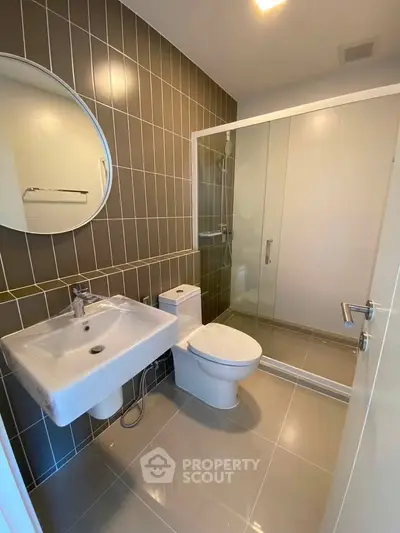 Modern bathroom with sleek design featuring a round mirror, glass shower, and stylish tile work.