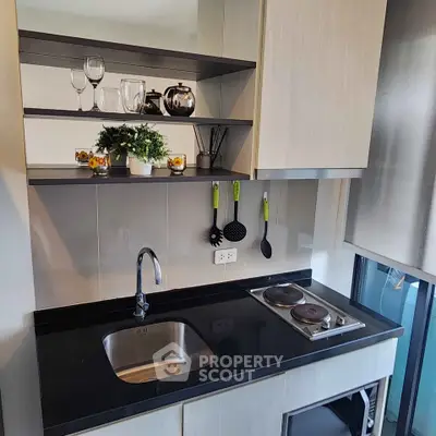 Modern kitchen with sleek black countertop and open shelving, featuring a compact electric stove and stylish decor.