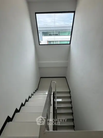 Modern staircase with large window offering natural light and view of contemporary building.