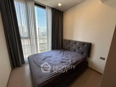 Modern bedroom with large window and city view, featuring a stylish bed and elegant curtains.