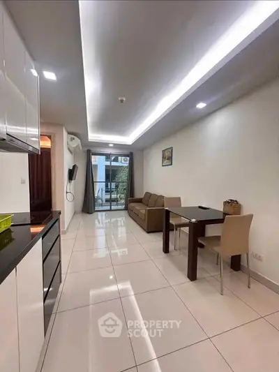 Modern open-layout living room with sleek kitchen and dining area, featuring contemporary furniture and bright lighting.