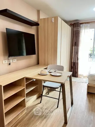 Modern studio apartment with wooden furniture and wall-mounted TV, featuring a cozy workspace and natural light.