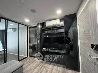 Modern living room with sleek black entertainment center and glass partition, featuring wood flooring and contemporary design.