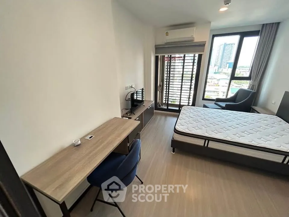 Modern bedroom with city view, featuring a desk, chair, and large window for natural light.
