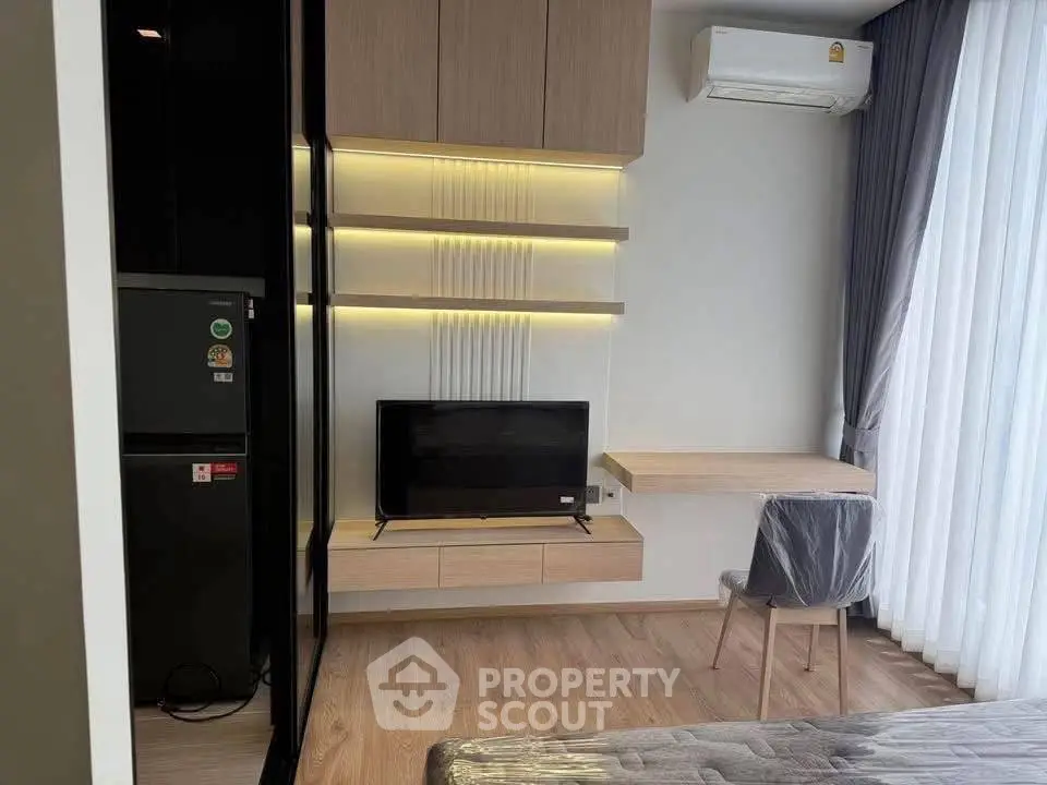 Modern living room with sleek furniture, wall-mounted TV, and natural light from large windows.