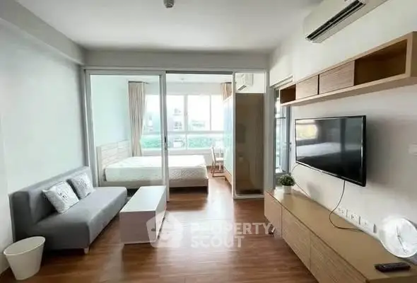 Modern studio apartment with open layout, featuring a cozy living area and a bright bedroom separated by glass doors.