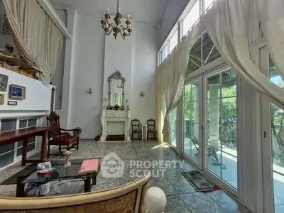 Elegant living room with high ceilings, chandelier, and large windows opening to a garden view.