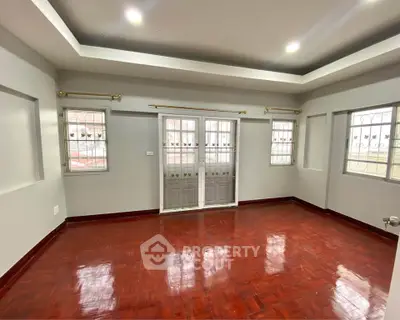 Spacious empty room with wooden flooring and large windows, ideal for customization.