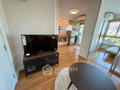 Modern living room with TV, open kitchen, and wooden flooring in a bright apartment.