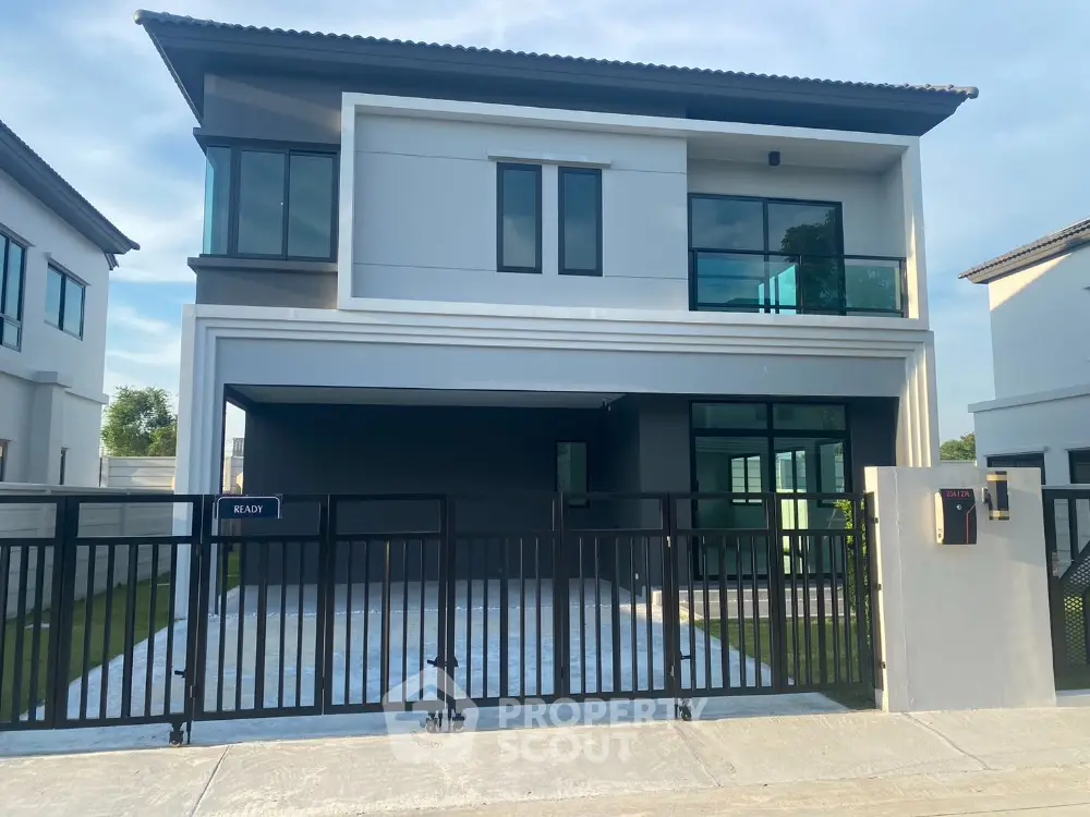 Modern two-story house with sleek design and gated driveway in suburban neighborhood.
