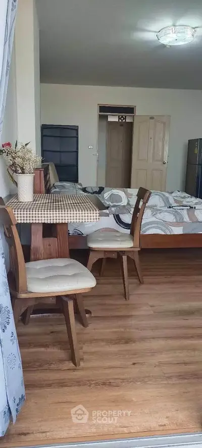 Cozy bedroom with wooden flooring and dining area, featuring a comfortable bed and stylish chairs.