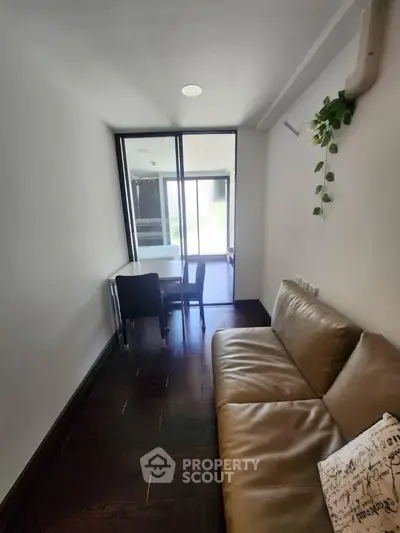 Cozy small living room with modern sofa and dining area, natural light from large window.