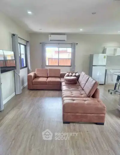 Spacious living room with modern brown sofas and large windows, featuring a sleek open kitchen layout.