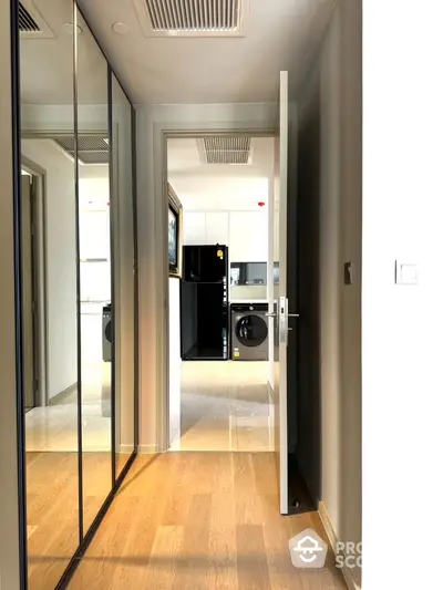 Modern apartment hallway with mirrored closet doors and view into kitchen with appliances.