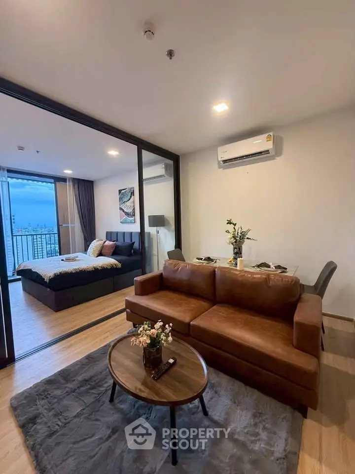 Modern open-plan living room with leather sofa and city view from bedroom balcony.