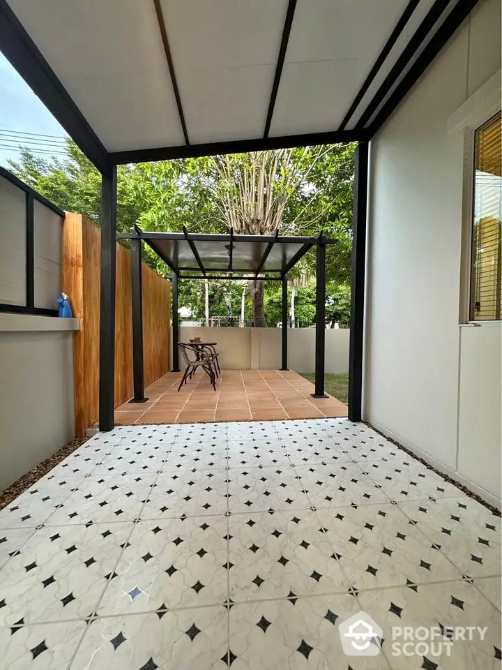 Modern patio with tiled flooring and outdoor seating area under a pergola, surrounded by greenery.