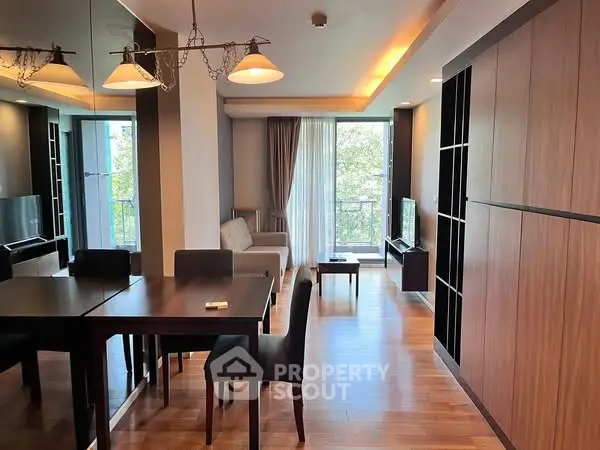 Modern living room with wooden flooring and stylish furniture, featuring a large window with natural light.