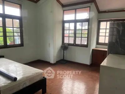 Spacious bedroom with large windows and wooden flooring in a serene residential area.